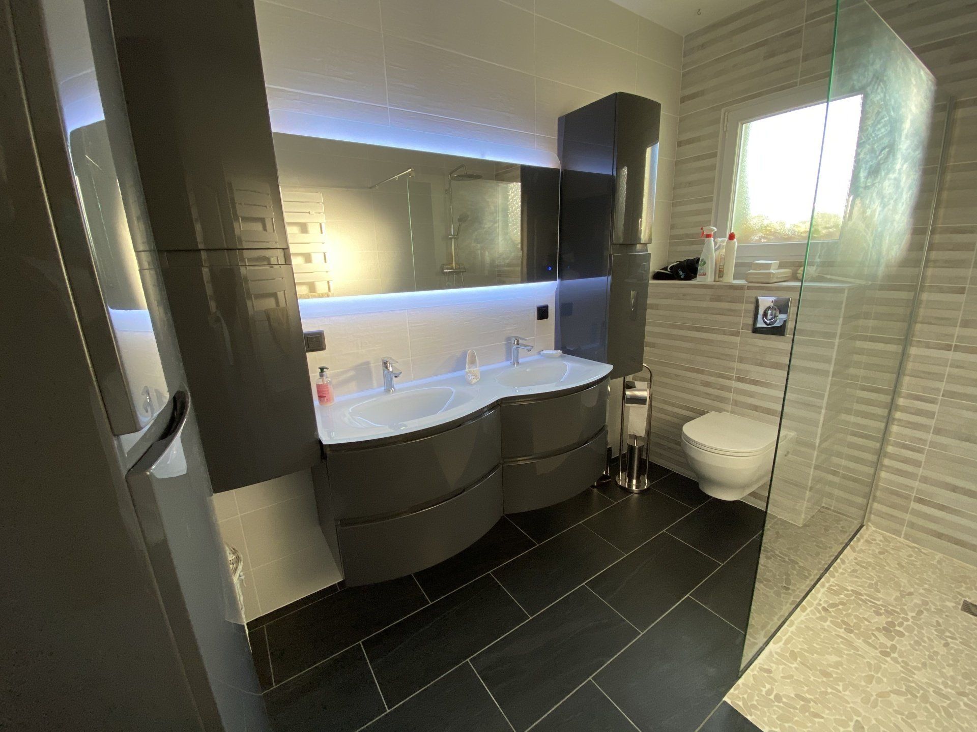 Salle de bains moderne avec meuble-lavabo double vasque, miroir, toilettes et grande douche carrelée.