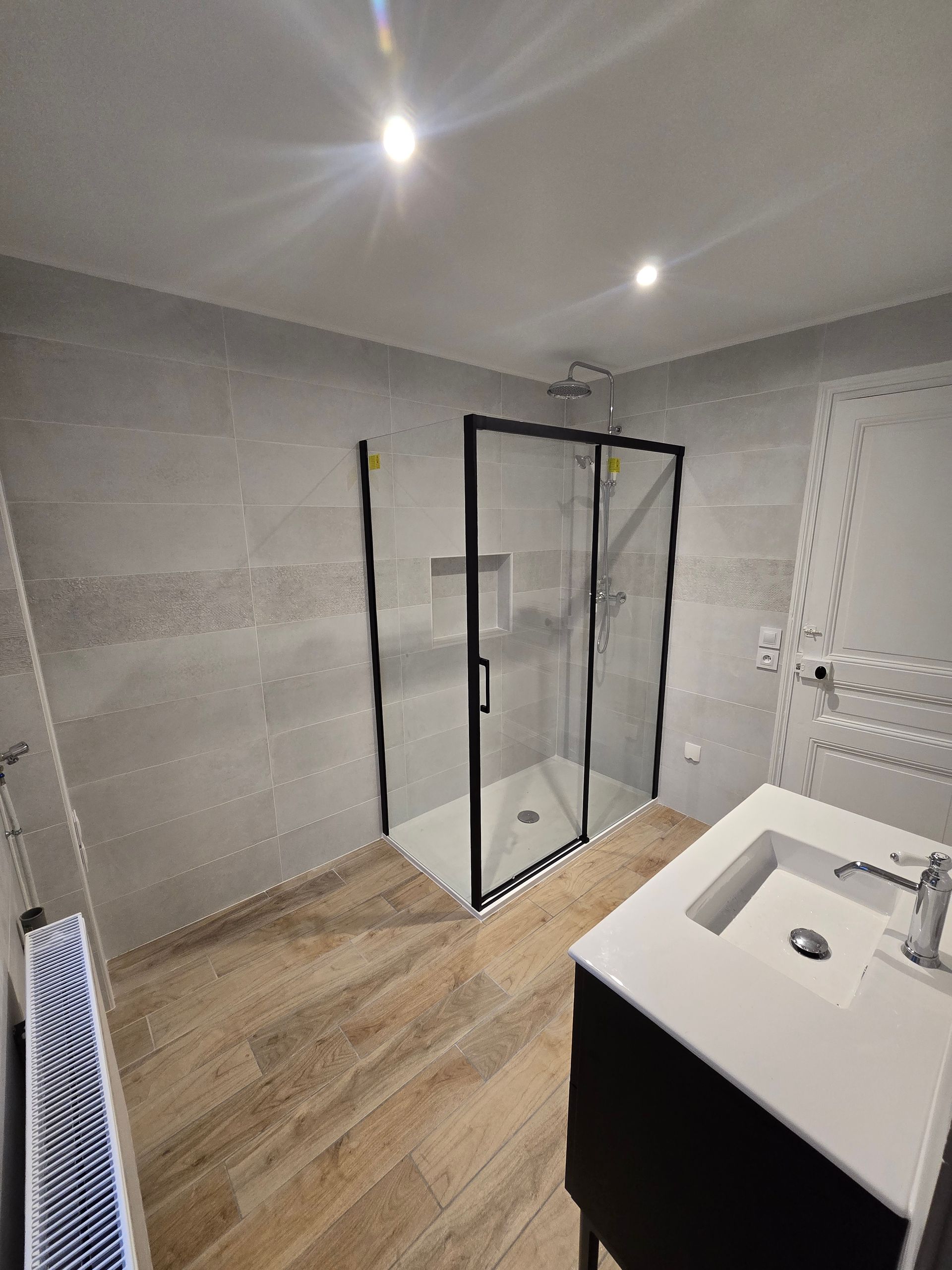 Une salle de bains moderne avec des murs carrelés gris, une douche à l'italienne à cadre noir.