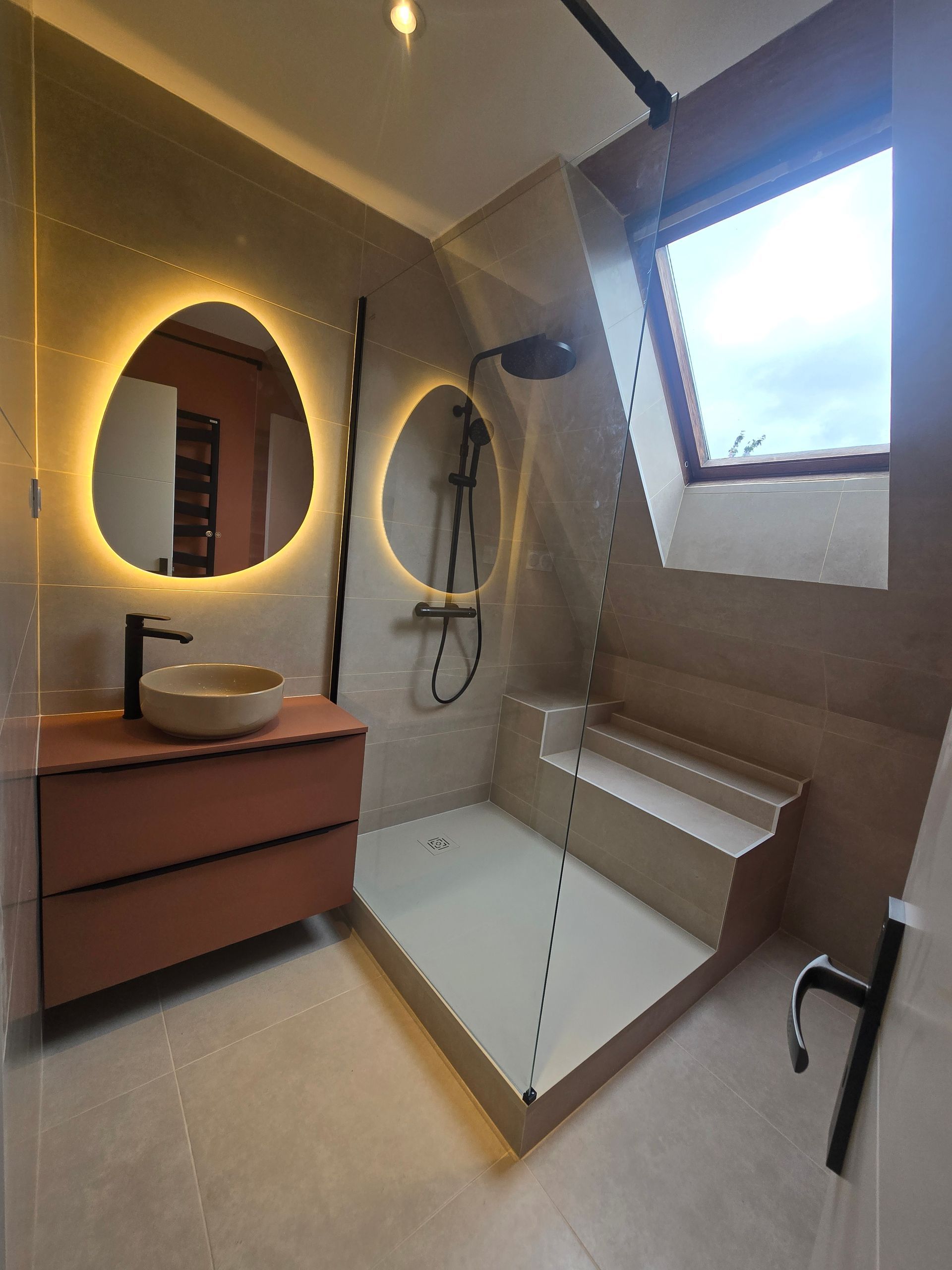 Salle de bains moderne avec un lavabo couleur pêche, deux miroirs rétroéclairés aux formes organiques.