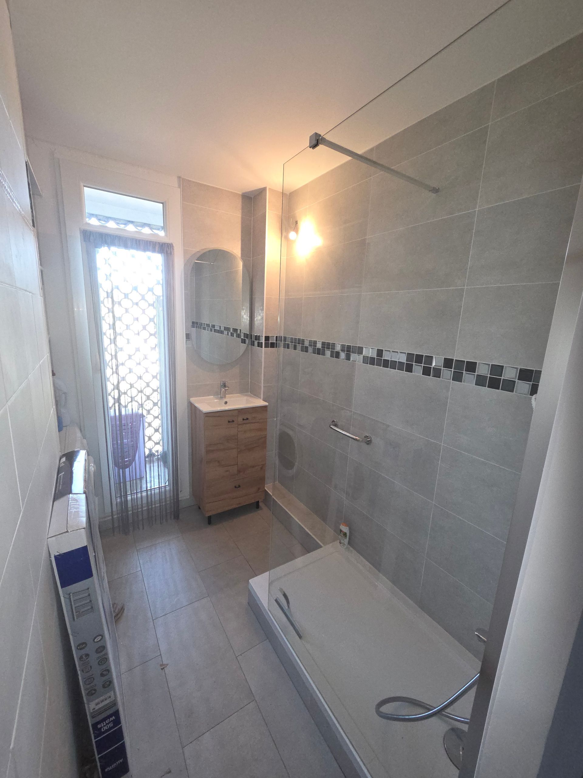Une salle de bains moderne comprend une douche à l'italienne carrelée, un lavabo en bois avec miroir.
