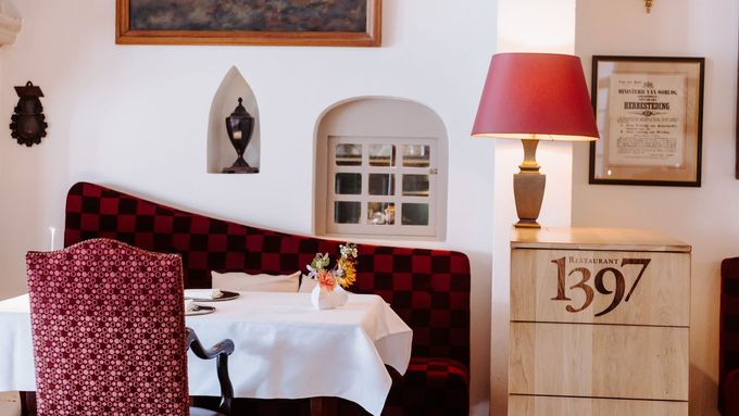Gezellig restaurantbankje met rood geblokte rugleuning, klein raam en een gedekte tafel om te dineren.
