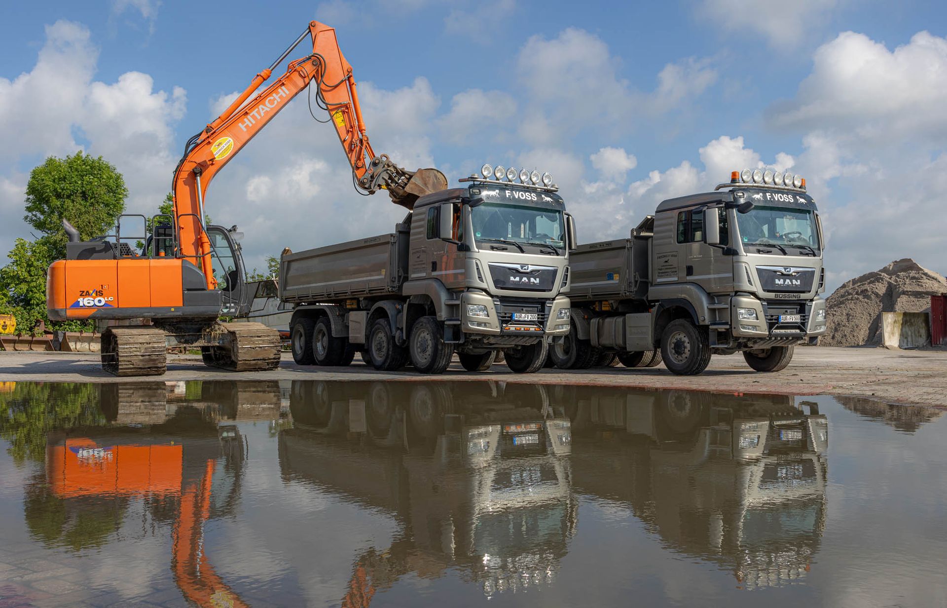Drei Muldenkipper stehen nebeneinander in einer Wasserpfütze.
