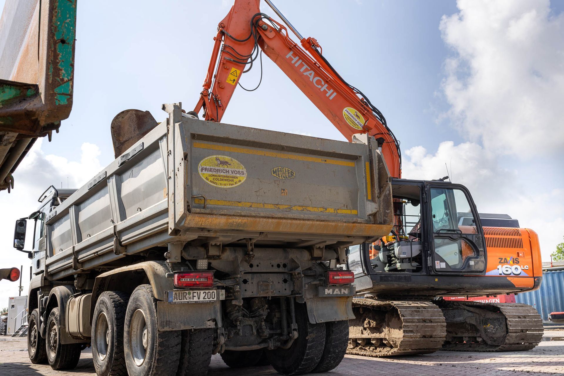 Ein Muldenkipper wird von einem Hitachi-Bagger mit Erde beladen.