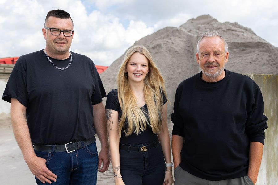 Drei Menschen stehen nebeneinander vor einem Erdhaufen.