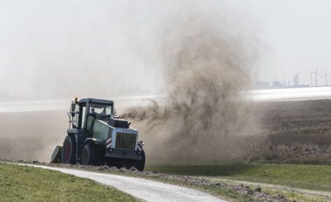 Ein Traktor pflügt ein Feld, wobei viel Staub aufwirbelt.