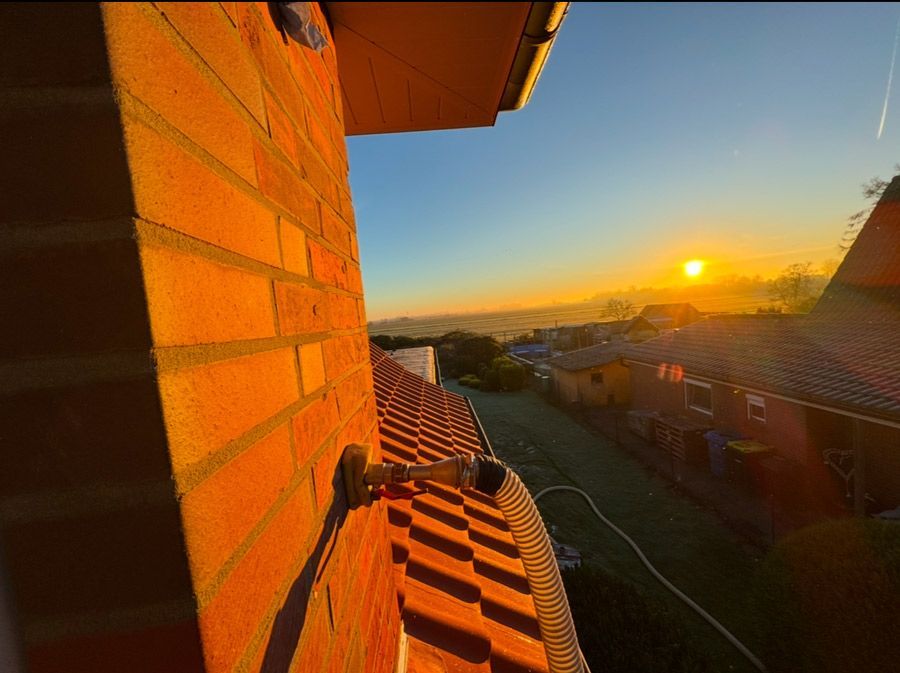 Eine Backsteinmauer mit einem daran befestigten Schlauch und einem Sonnenuntergang im Hintergrund.