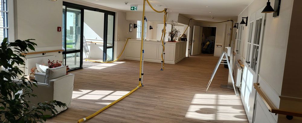 Leerer, sonnendurchfluteter Flur mit Holzboden, weißen Wänden, offenen Türen und einer gelben Absperrung