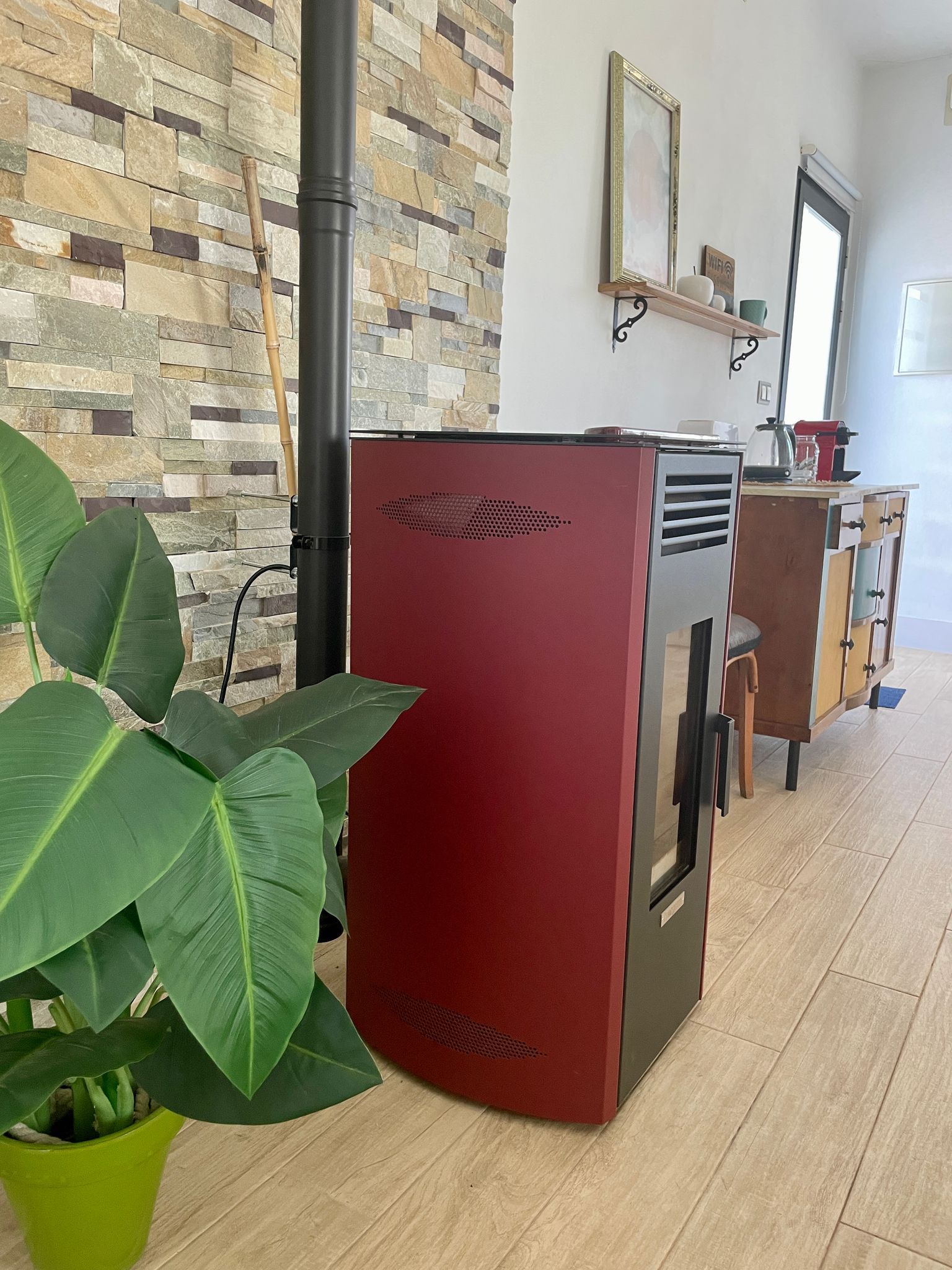 Una estufa roja está ubicada en una sala de estar al lado de una planta en maceta.