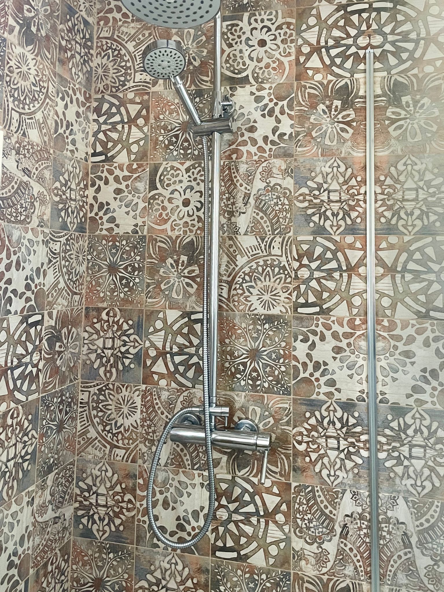 Una ducha con una pared de azulejos estampados y un cabezal de ducha.