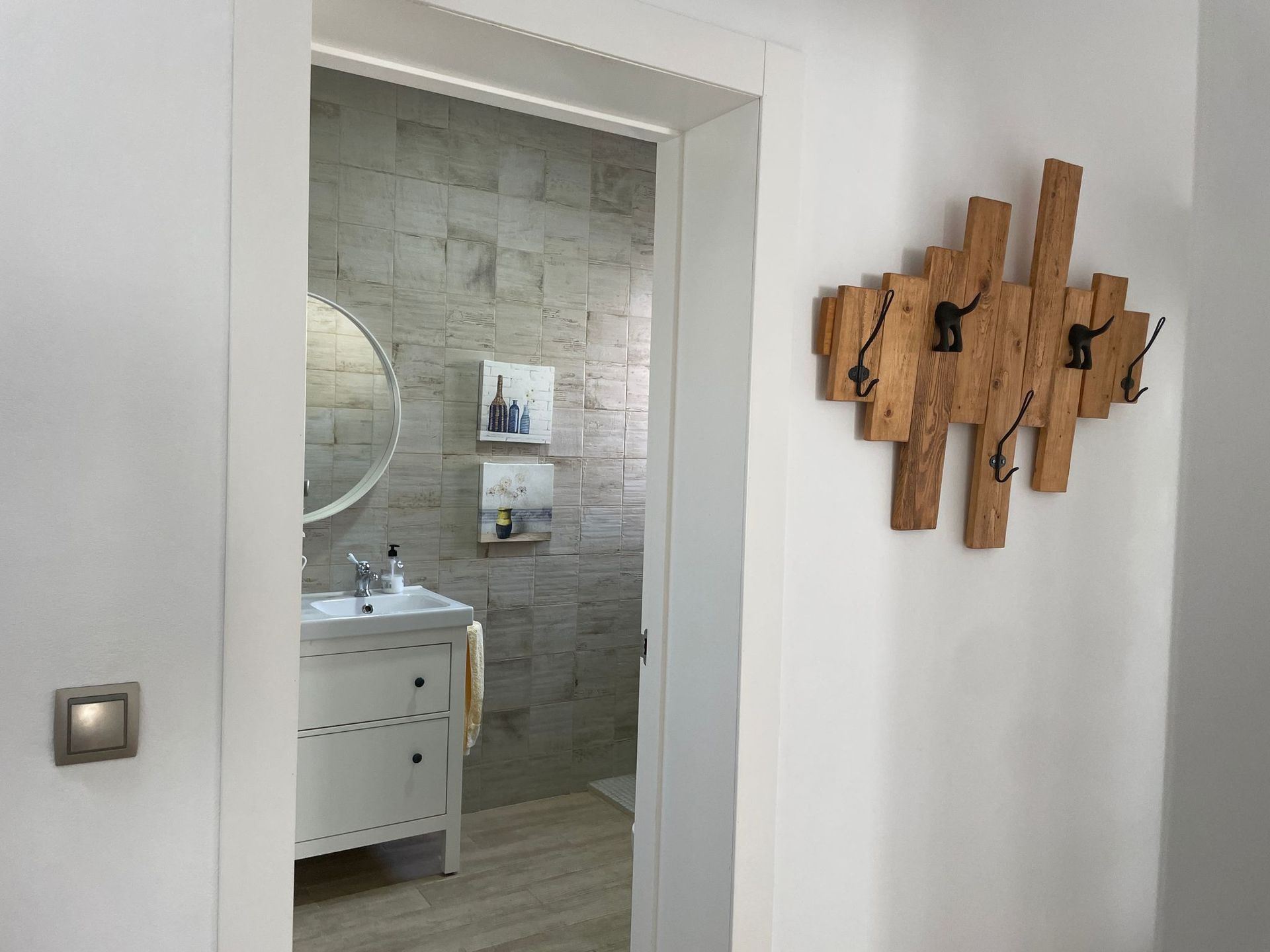 Un baño con lavabo, espejo y ganchos de madera en la pared.