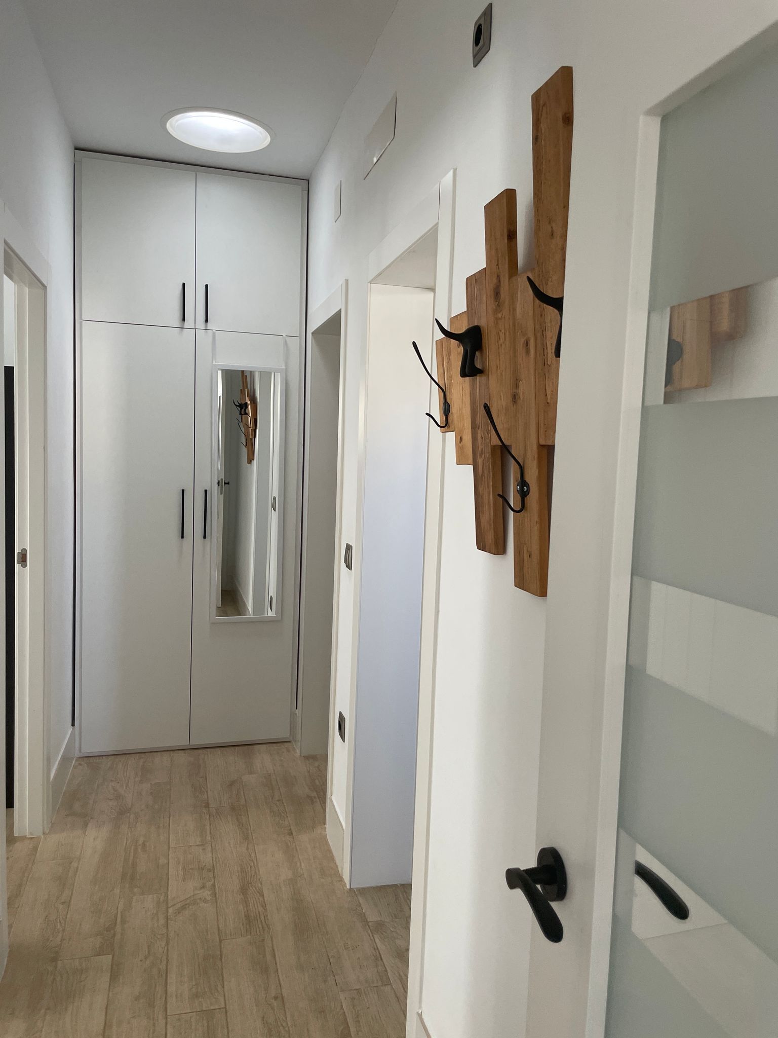 Un pasillo con paredes blancas y ganchos de madera en la pared.