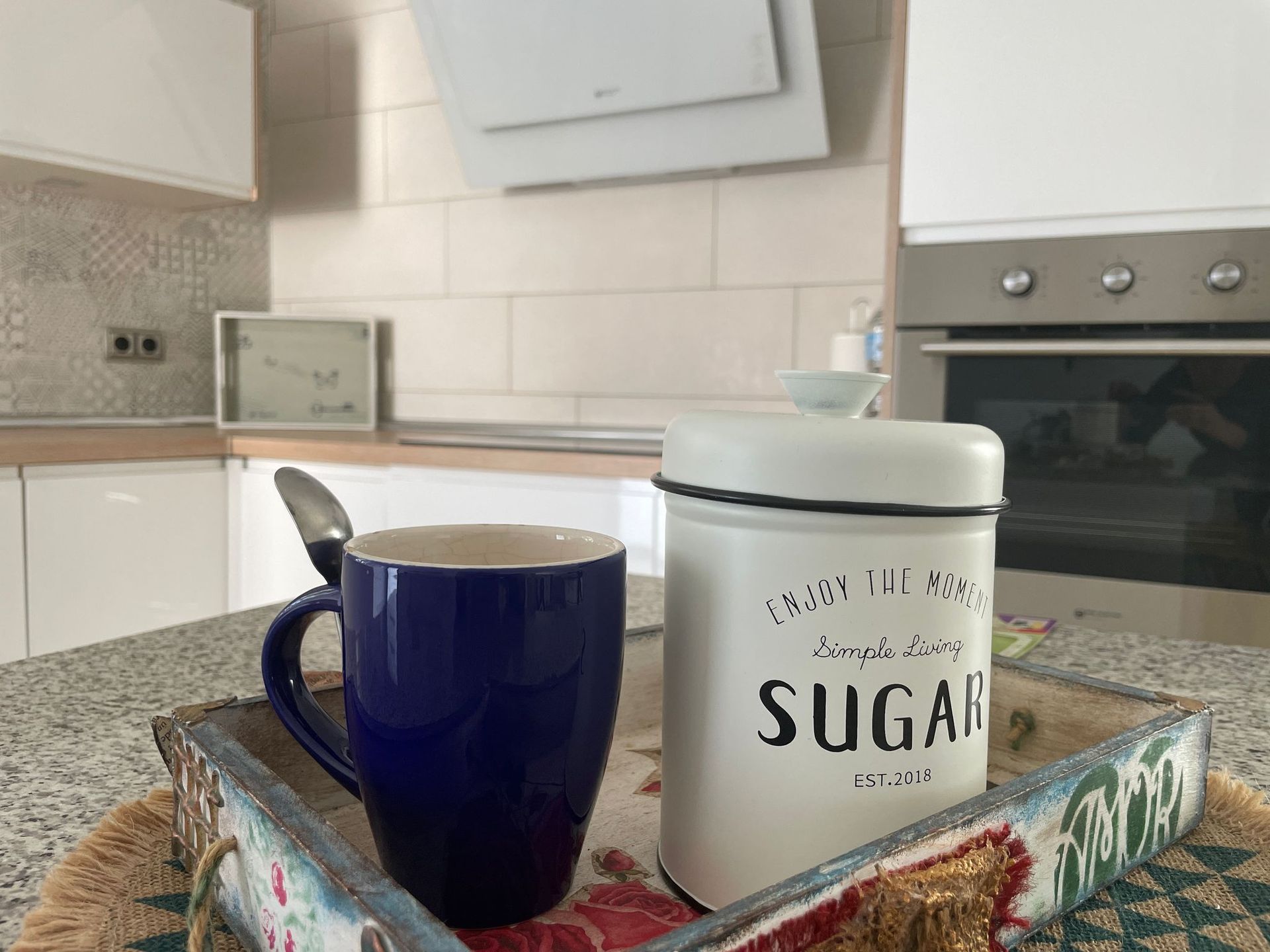 Una taza azul y una lata de azúcar blanca están en una bandeja en una cocina.
