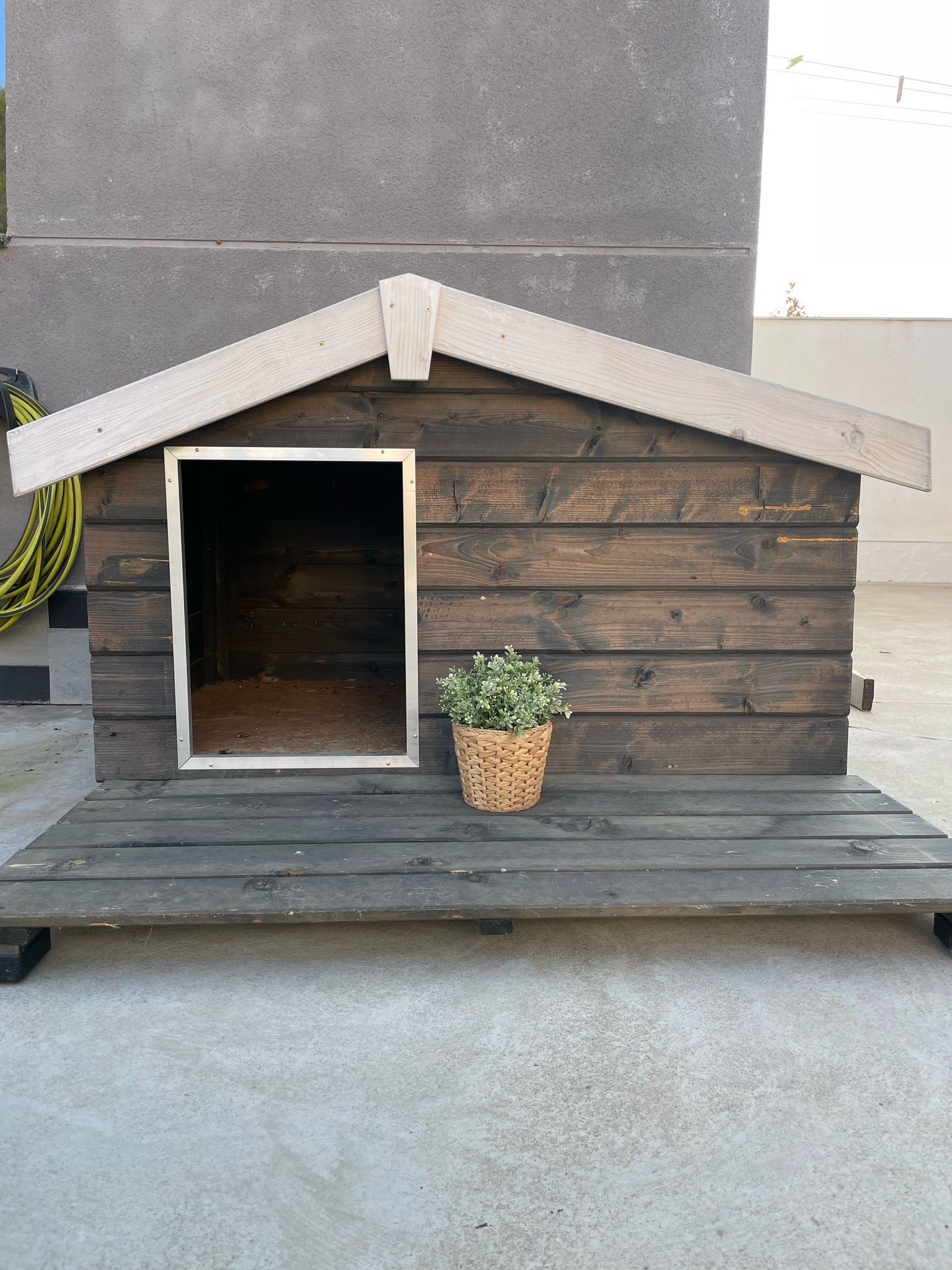 Una caseta de madera para perro con una planta en maceta delante de ella.