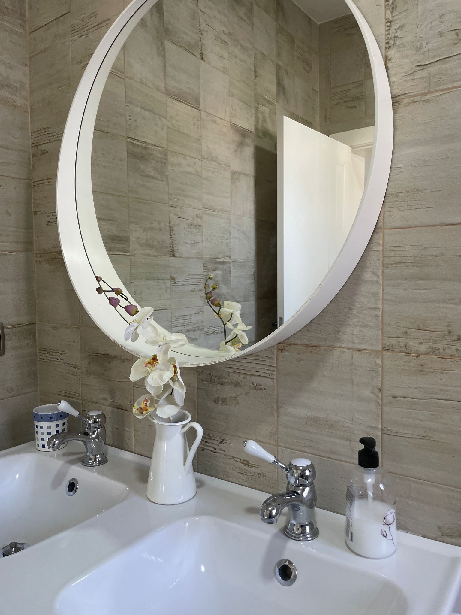 Un baño con dos lavabos y un espejo redondo.