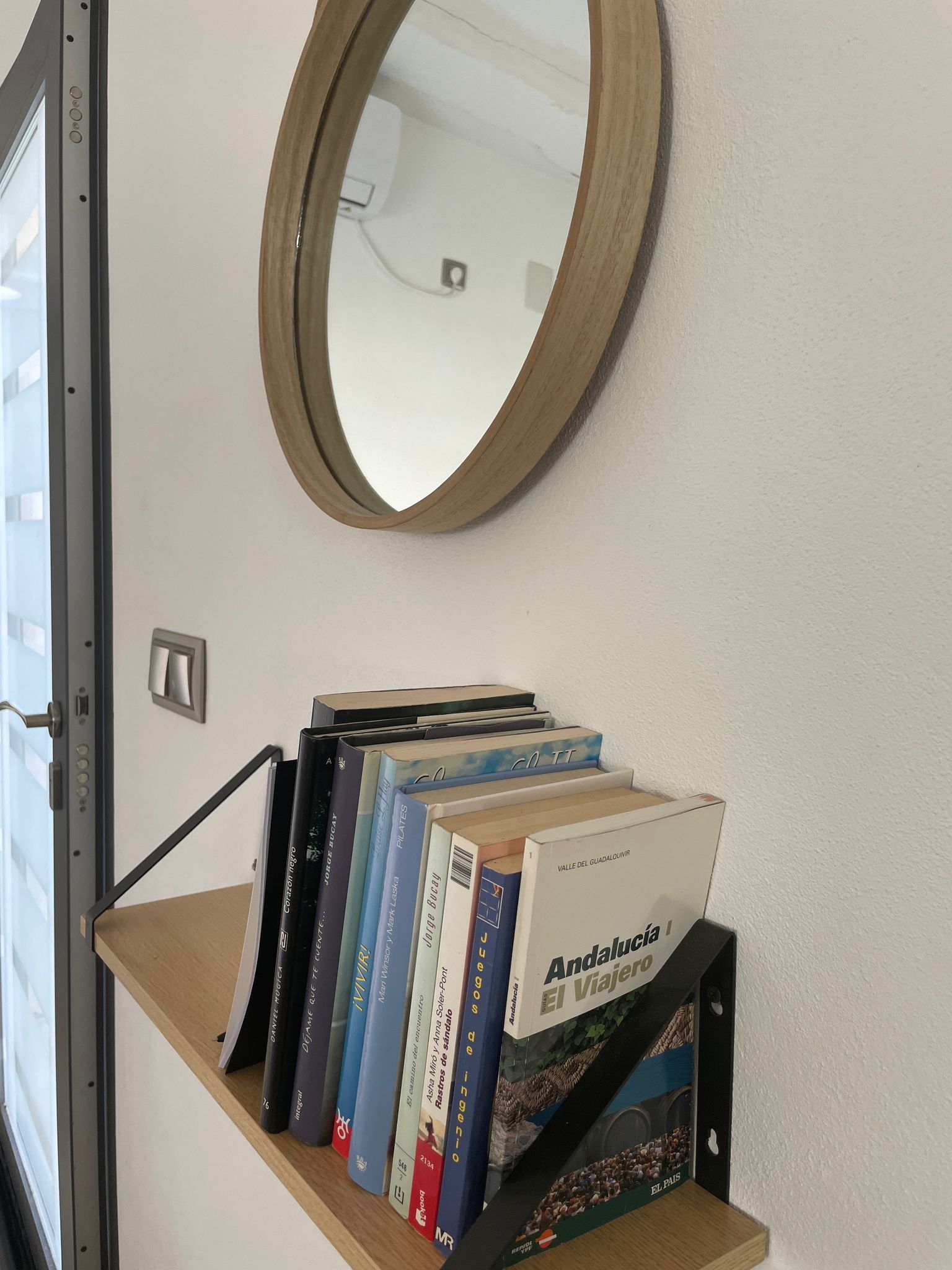 Un estante con libros y un espejo en la pared.
