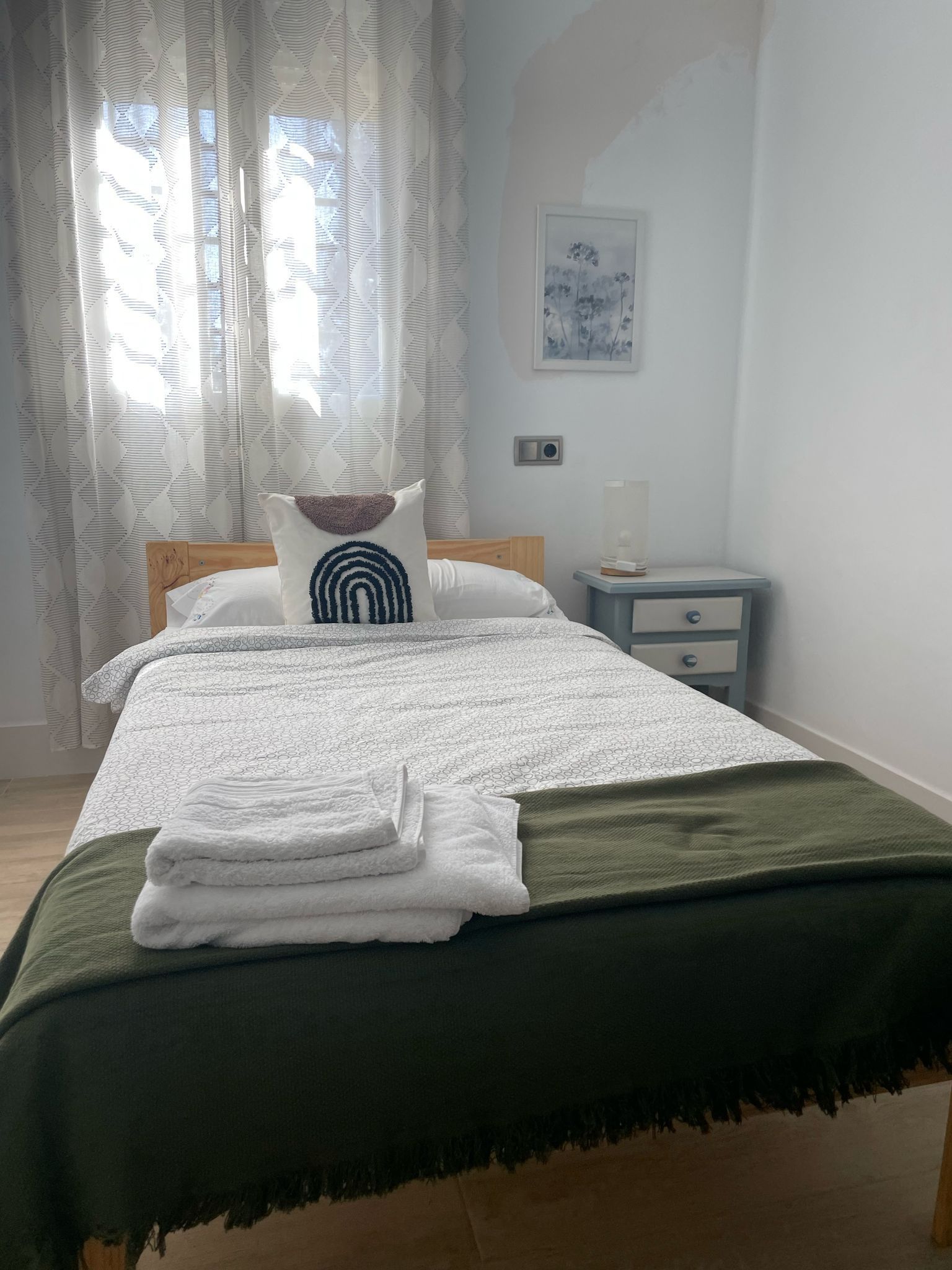 Un dormitorio con cama, mesita de noche y ventana.