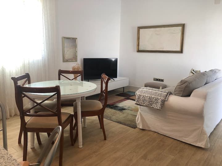 Una sala de estar con sofá, mesa, sillas y televisor de pantalla plana.