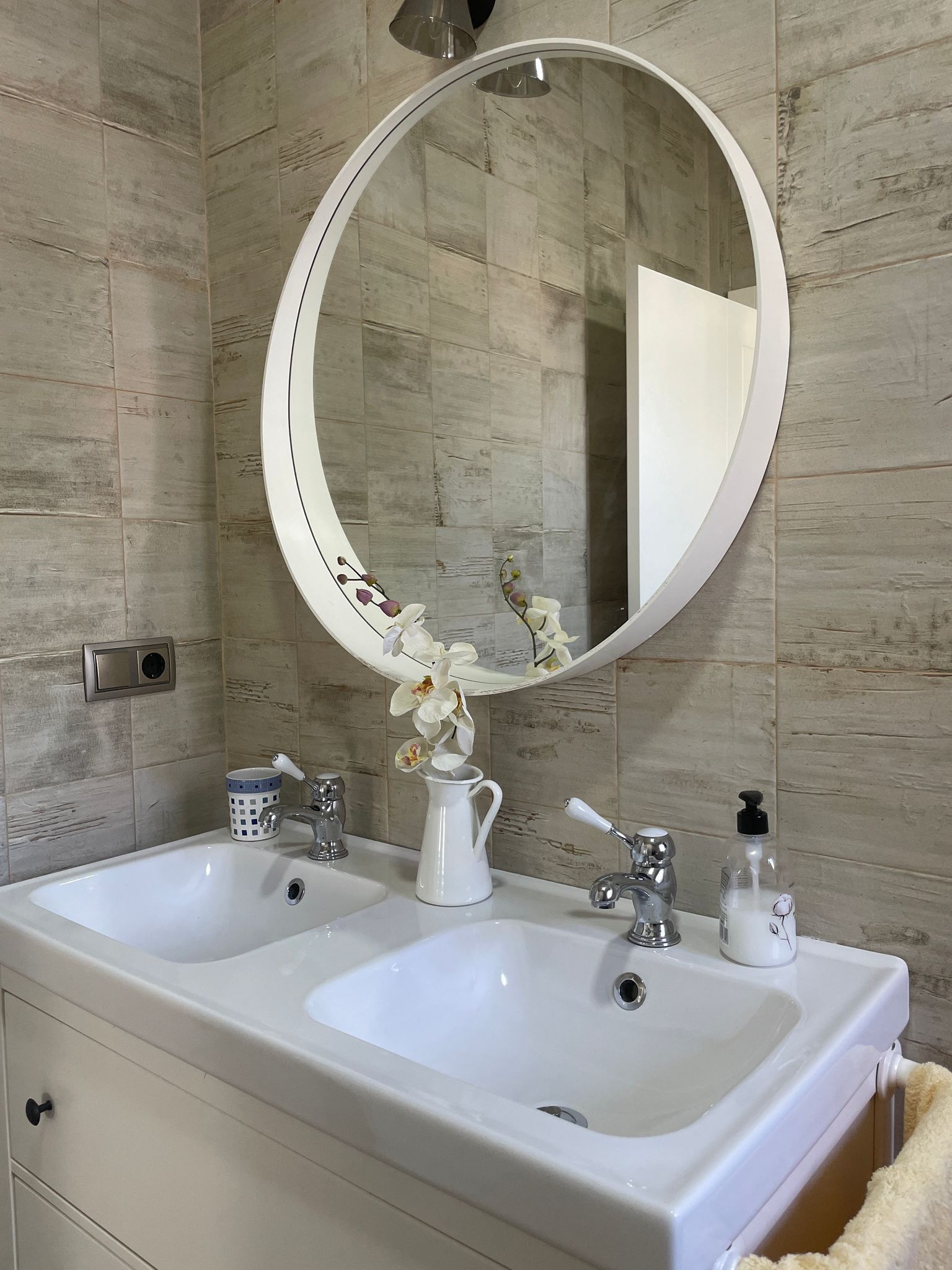 Un baño con dos lavabos y un espejo redondo.