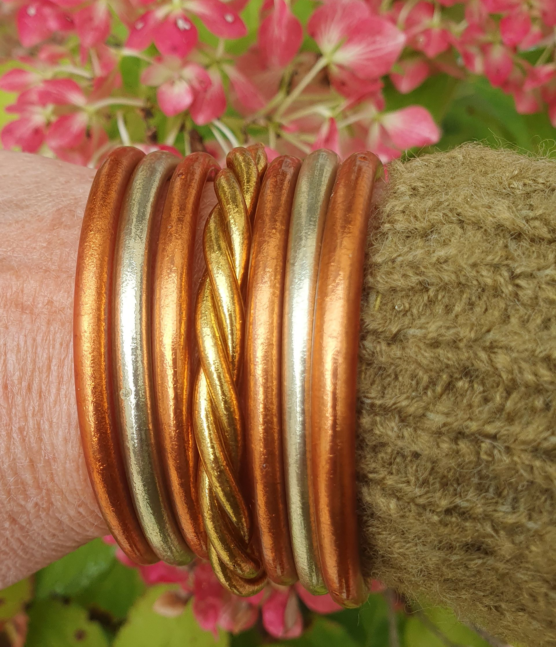 Gros plan sur un poignet orné de bracelets en cuivre, en argent et en or, à côté d'une manche en tricot vert.