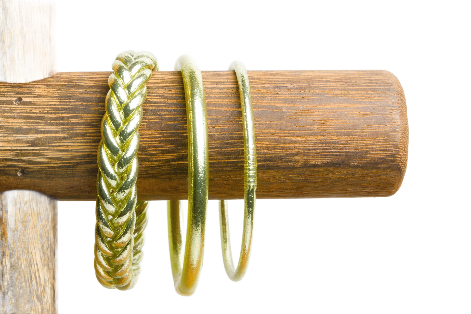 Trois bracelets en or sur une cheville en bois. Le bracelet de gauche est tressé.