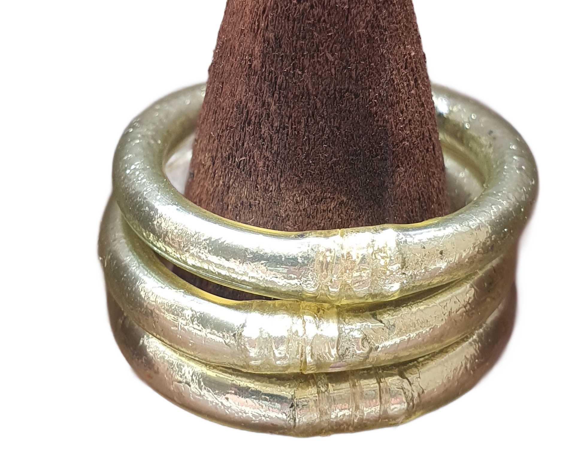 Trois bracelets argentés empilés sur une forme conique brune.
