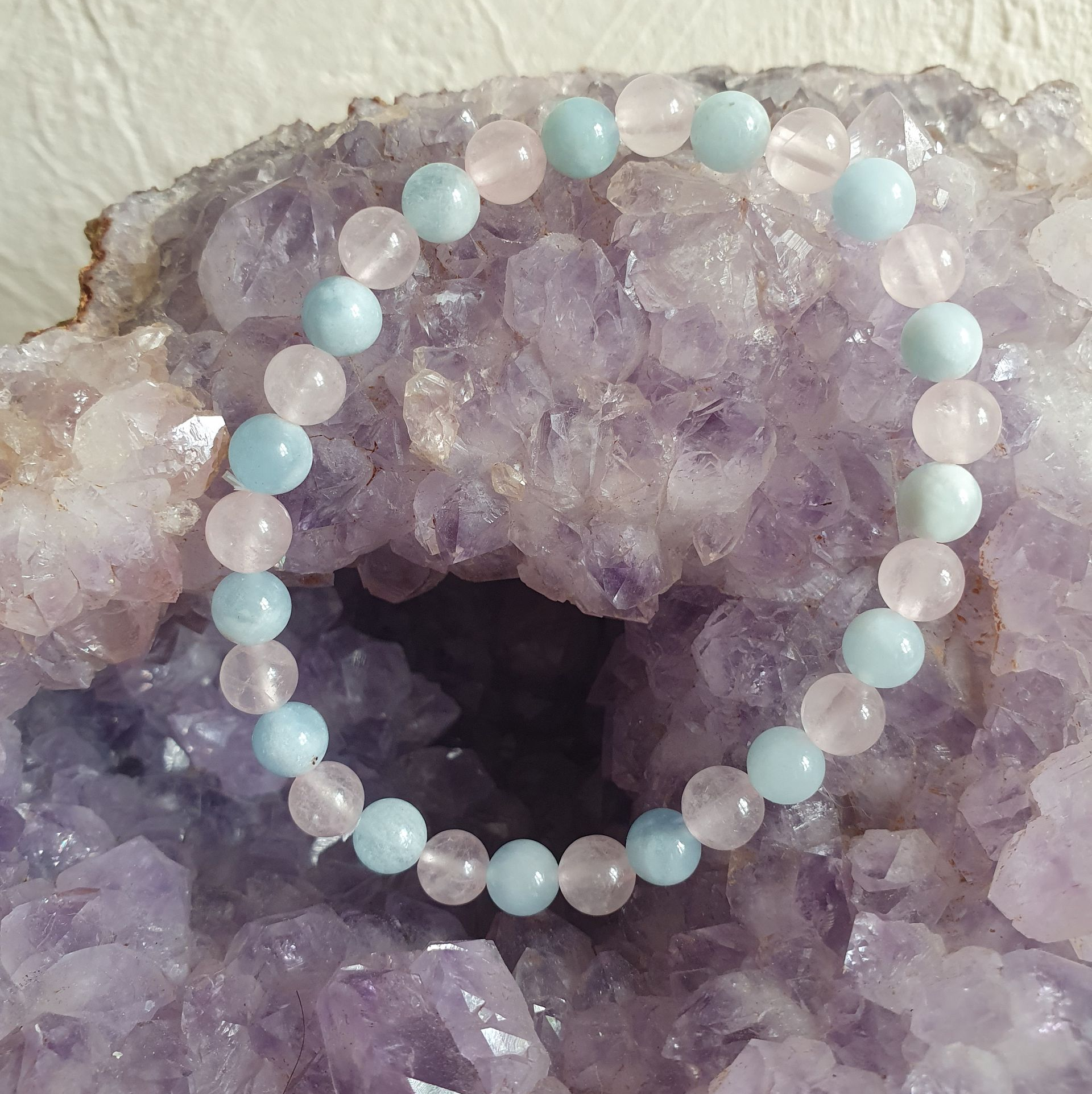 Un bracelet de perles composé de pierres précieuses rose pâle et bleues reposant sur une géode de cristal violet.