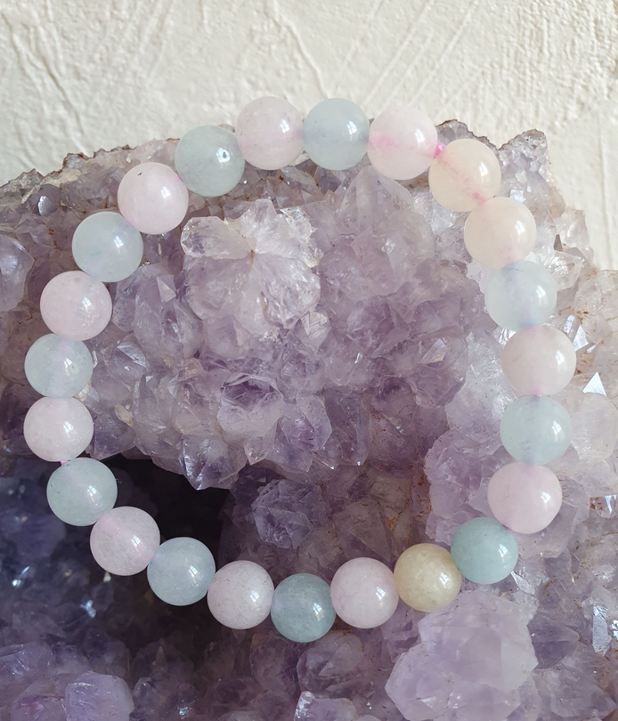 Bracelet de perles orné de pierres rose pâle et bleu-vert, posé sur une géode de cristal violet.