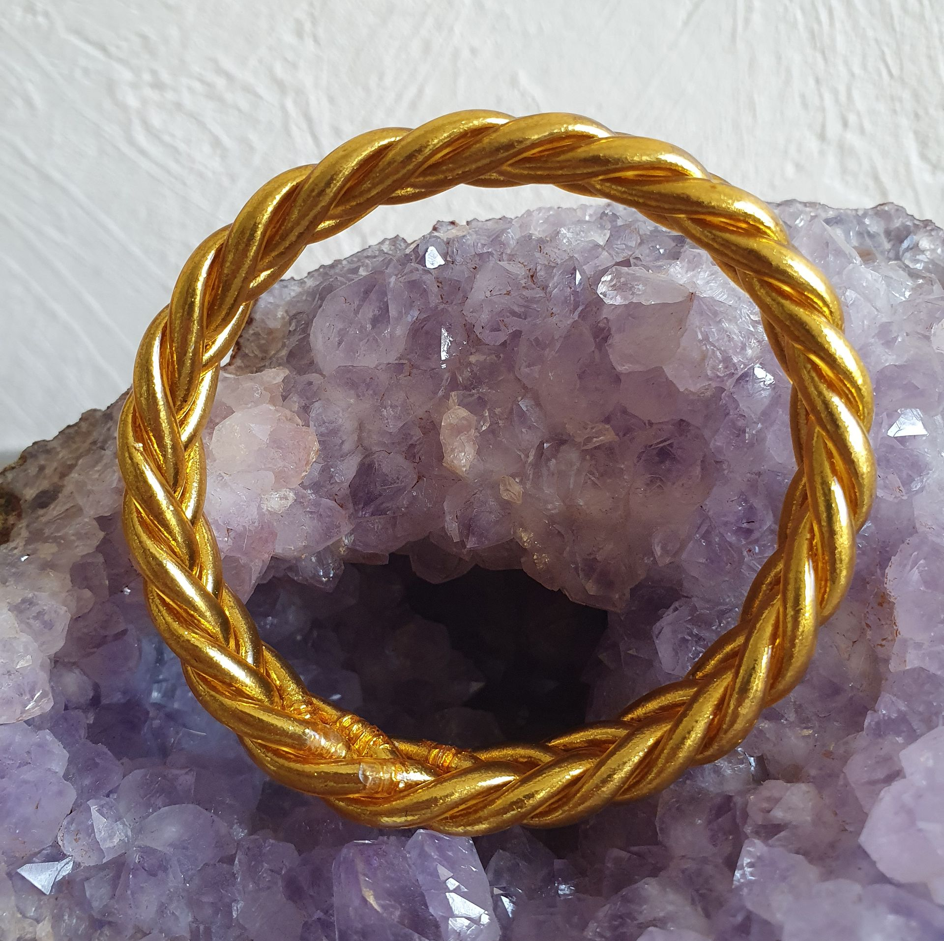 Bracelet en joncs tressés de couleur or sur fond de cristal violet.