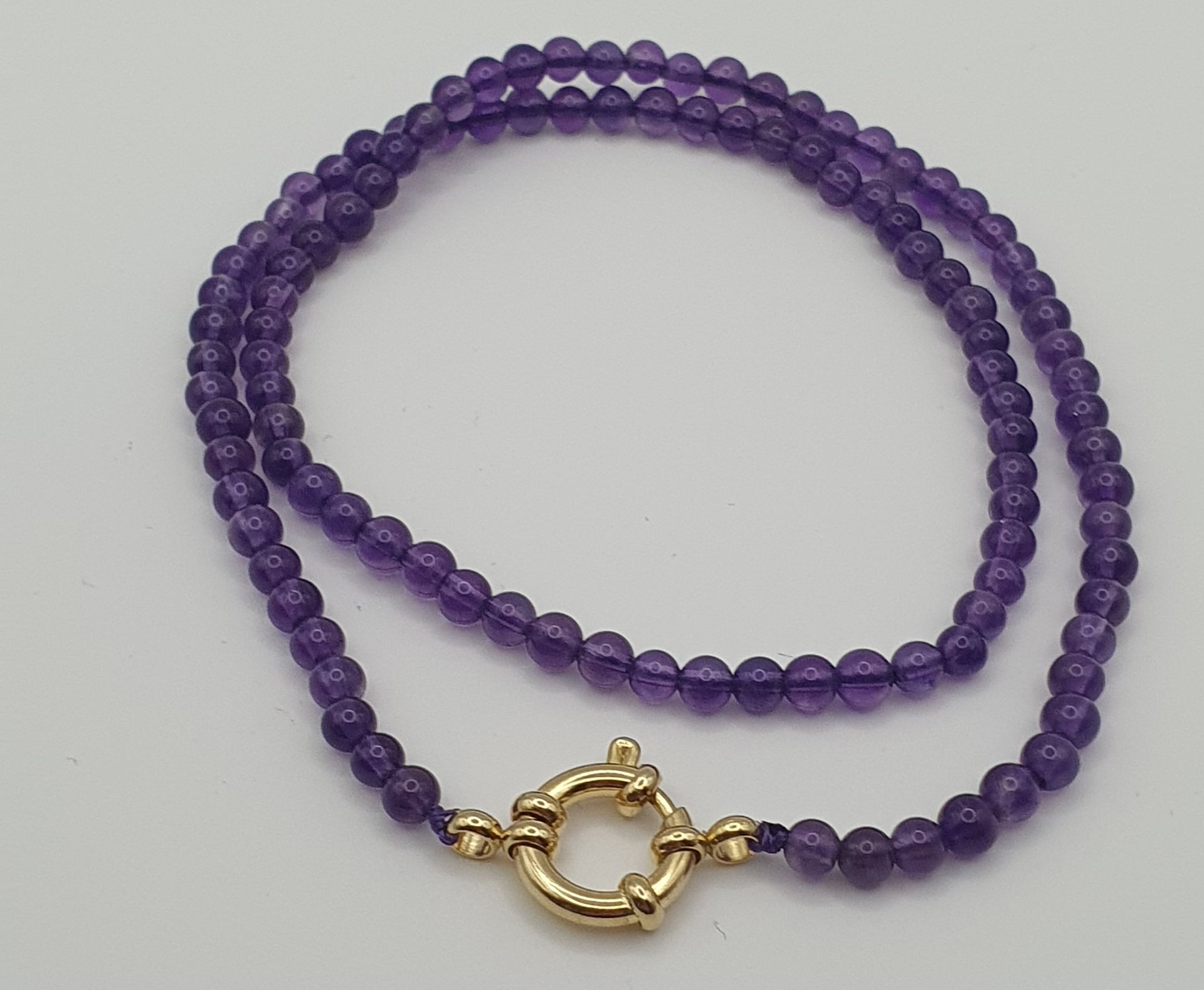 Collier de perles améthyste violet avec fermoir doré.