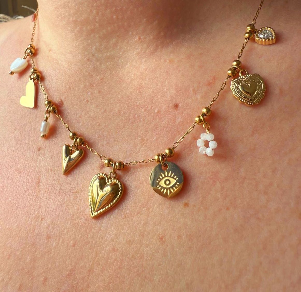 Collier en or orné de breloques en forme de cœur, d'œil et de fleur, porté autour du cou.