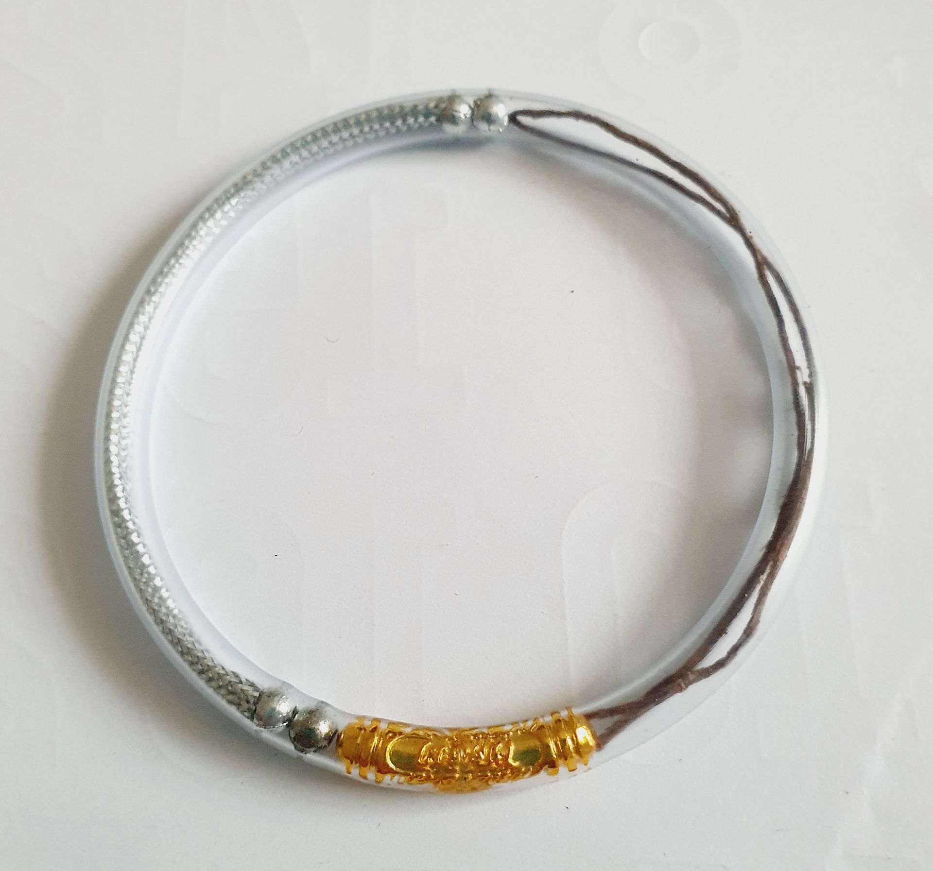 Bracelet en argent avec un cordon marron foncé, posé sur une surface blanche.
