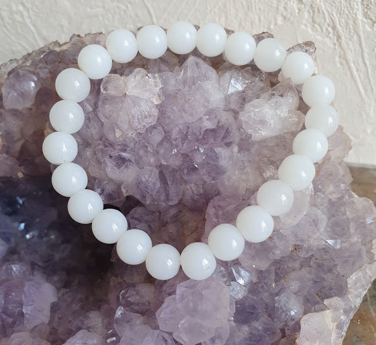 Bracelet de perles de jade blanches sur une géode de cristal d'améthyste violette.