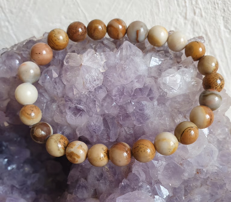 Bracelet de perles orné de pierres de jaspe aux tons terreux, sur un lit de cristaux d'améthyste violette.