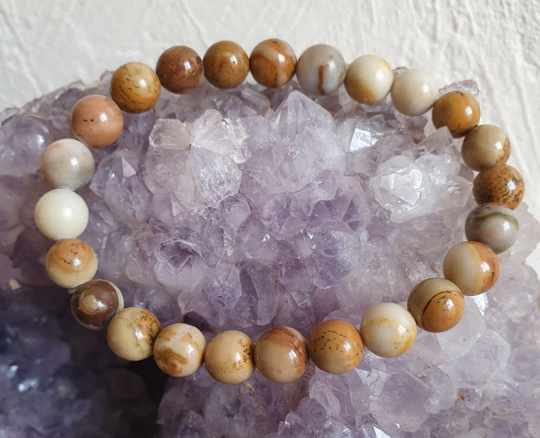 Bracelet de perles orné de pierres aux tons naturels reposant sur un cristal d'améthyste violette.