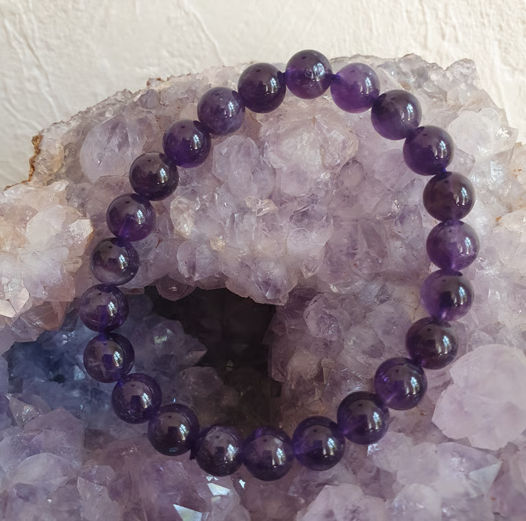 Bracelet de perles d'améthyste violettes posé sur un lit de cristaux d'améthyste.