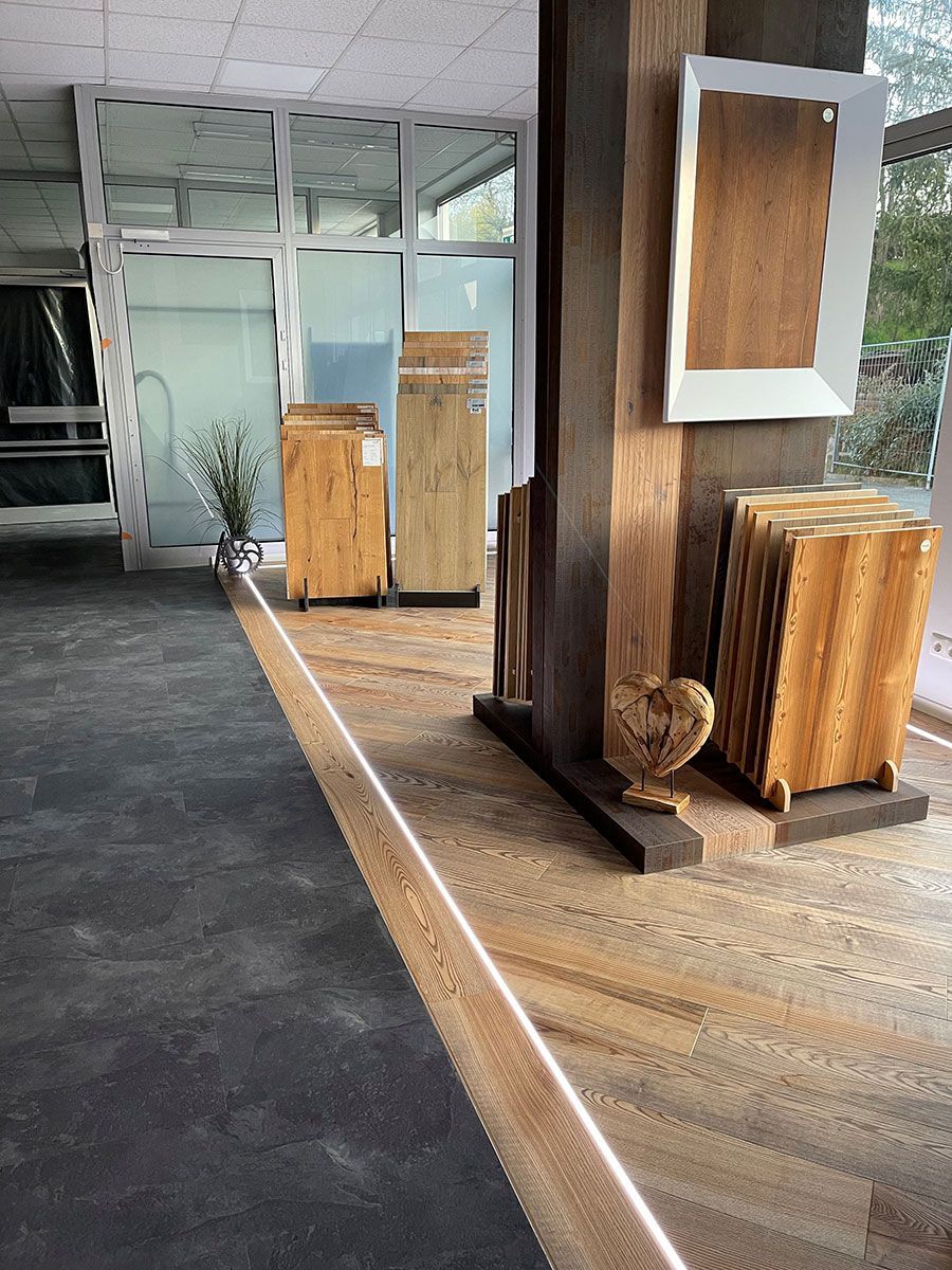 Moderne Lobby mit Holzsäulen, geflochtenen Hockern und gläsernen Eingangstüren, die sich zu einem dunklen Außengang öffnen.