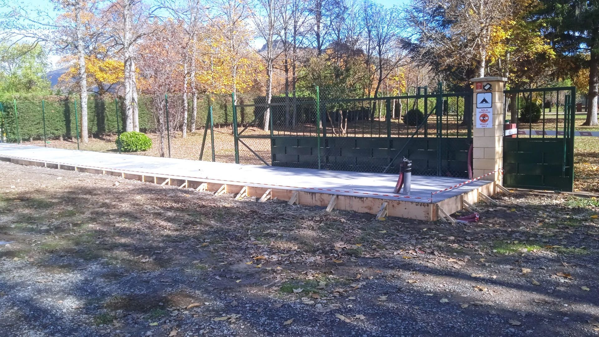 Entrada a un parque con portón de hormigón y grifo de agua. Árboles y follaje al fondo.