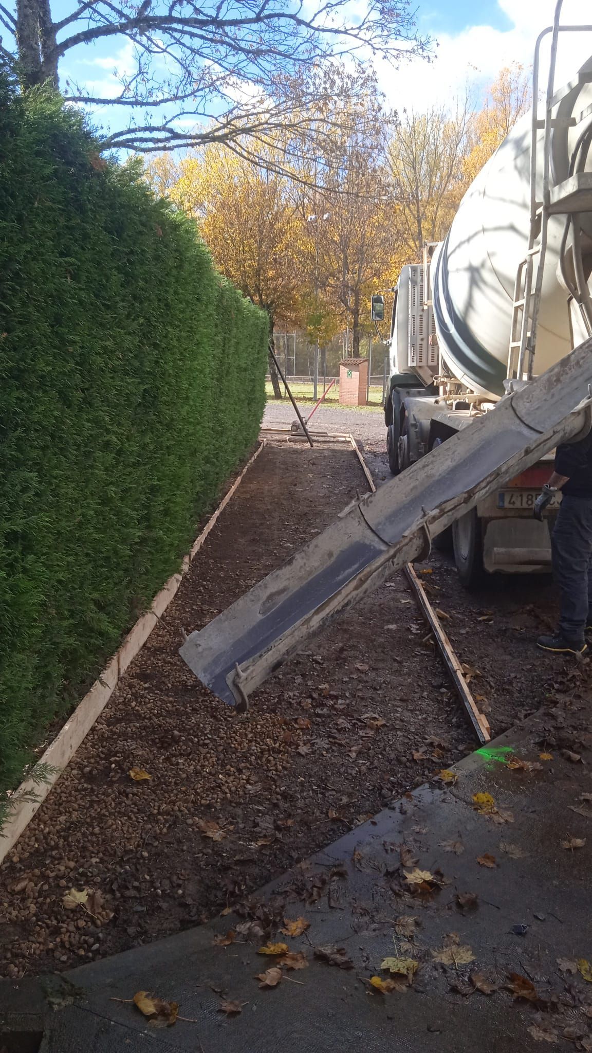 El hormigón se vierte desde un camión sobre un lecho de grava junto a un seto alto y verde.