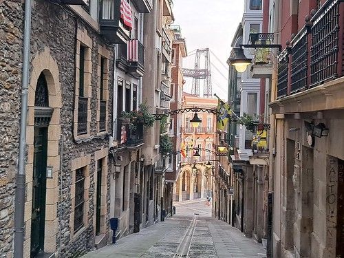 Un callejón estrecho entre dos edificios con un puente al fondo.