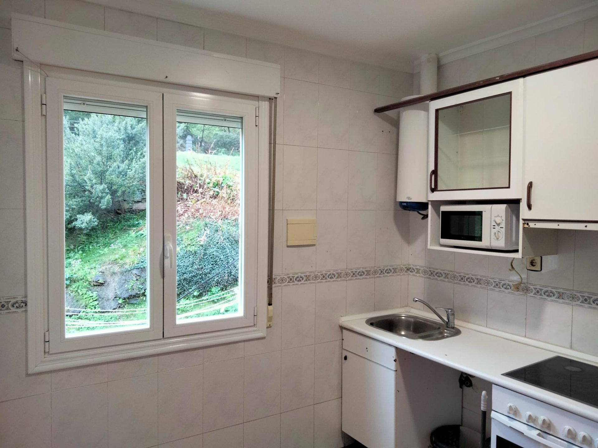 Una cocina con fregadero, estufa, microondas y dos ventanas.