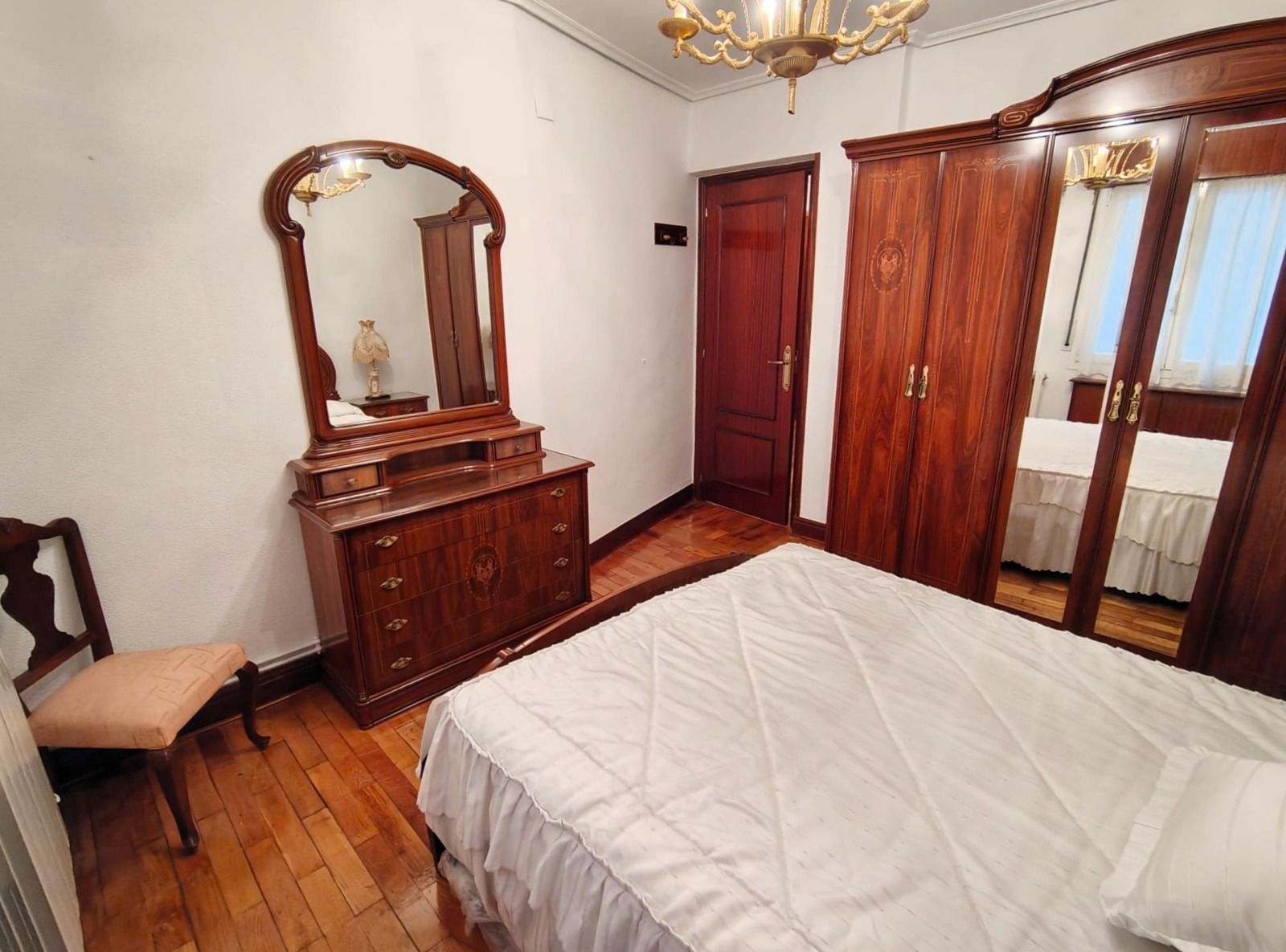 Un dormitorio con una cama, cómoda, espejo y silla.
