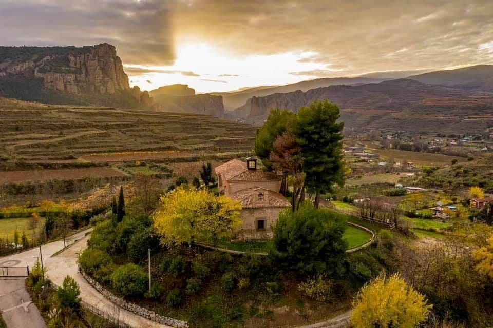 Una vista aérea de una casa en la cima de una colina con una puesta de sol al fondo.