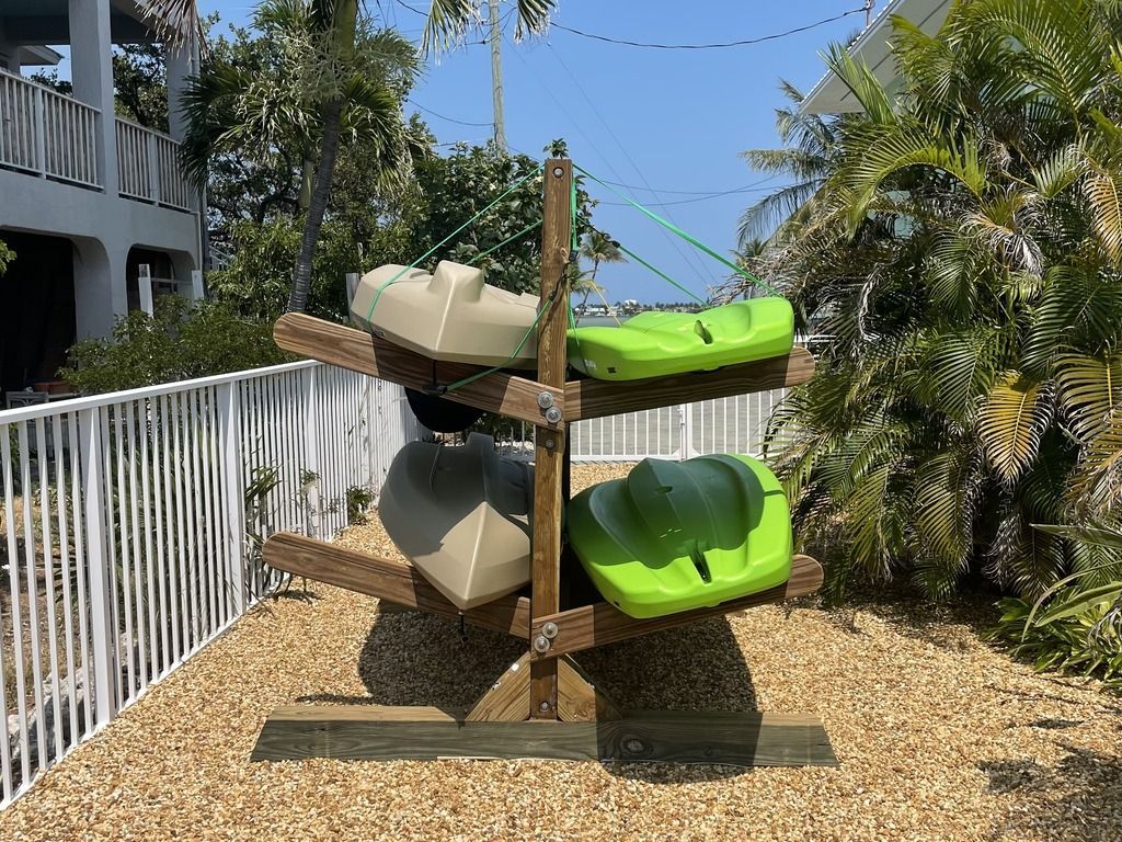Kayak rack holding four kayaks, two green and two beige, in a sunny outdoor setting.