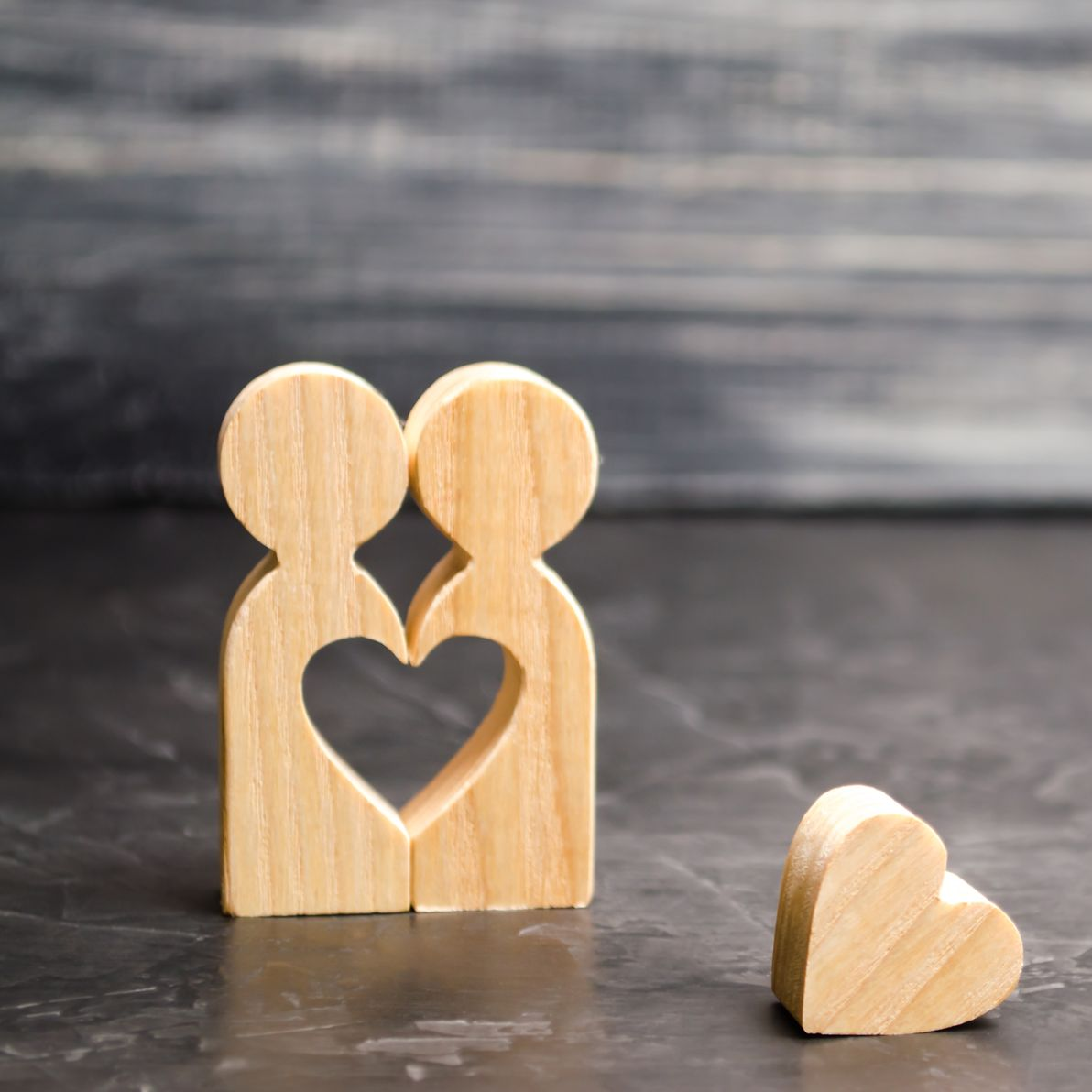 Puzzle en bois en forme de cœur avec deux figurines et un petit cœur sur une surface grise