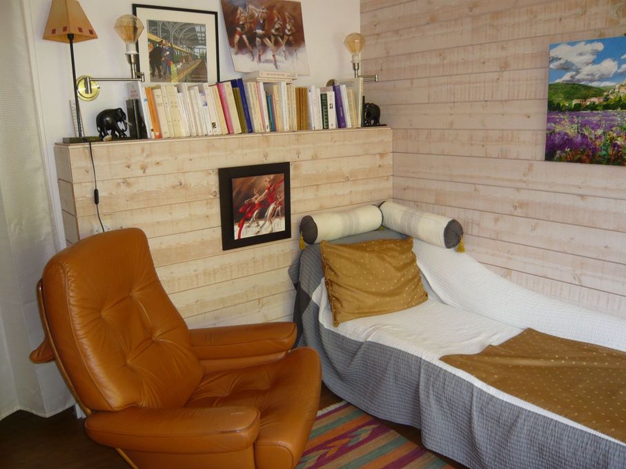 Chambre confortable avec fauteuil inclinable beige, méridienne blanche, livres sur une étagère et tableaux encadrés.