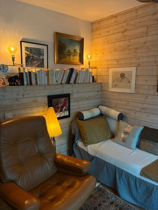 Chambre confortable avec fauteuil inclinable beige, méridienne blanche, livres sur une étagère et tableaux encadrés.