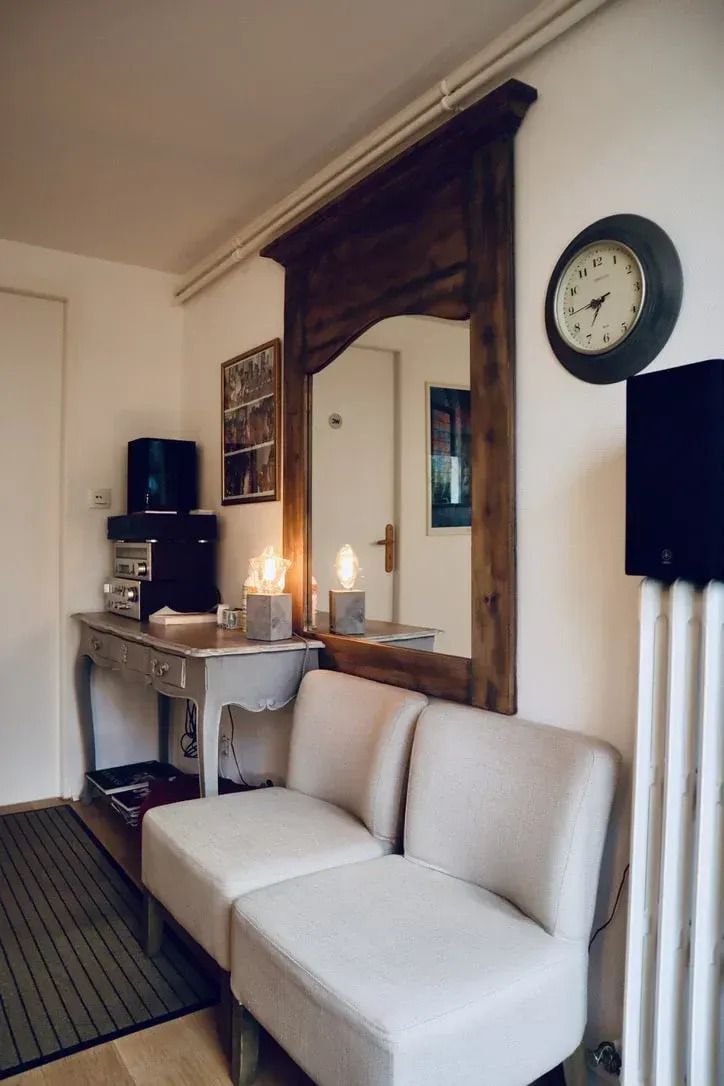 Salon cosy avec canapé crème, miroir orné, console, horloge murale et décoration éclairée à la bougie