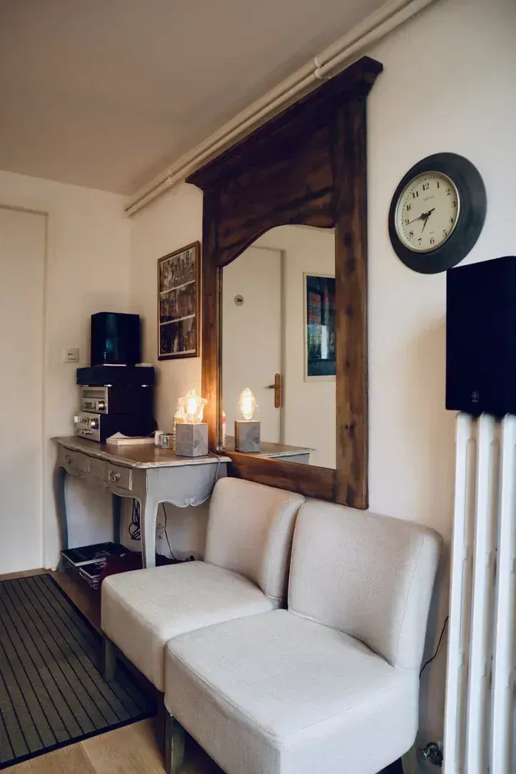 Salon cosy avec un canapé blanc, un miroir orné, une console et une horloge murale.