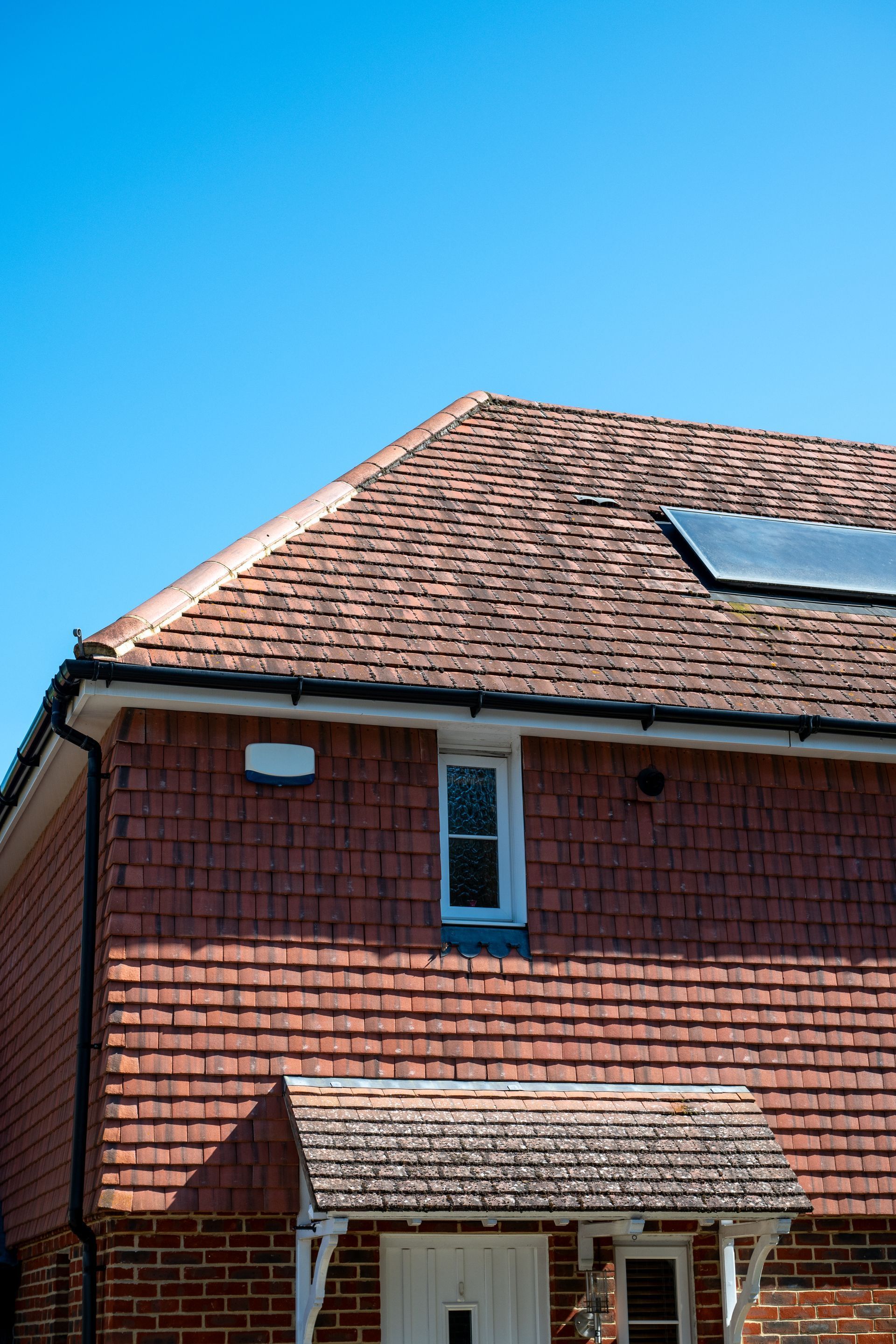 Red brick house with a tiled roof and skylight against a clear blue sky