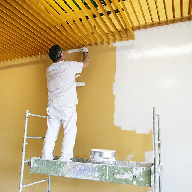 Peintre en bâtiment en train de peindre un mur en blanc sur un échafaudage